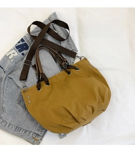 Detail of yellow canvas tote bag with brown leather handles on denim jacket backdrop