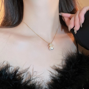 Close-up of a gold necklace featuring a lustrous white pearl pendant on a female model