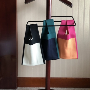 Three colorful knitted tote bags with unique single handle design hanging on a wooden rack