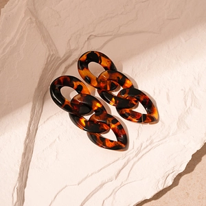 Detailed view of tortoiseshell acrylic chain link earrings on a white stone background