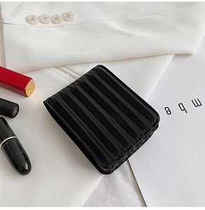 Detail of black pleated mini makeup pouch with mirror and red lipsticks on white blazer