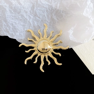Macro shot of sun-shaped golden brooch with wavy rays and polished mirror finish