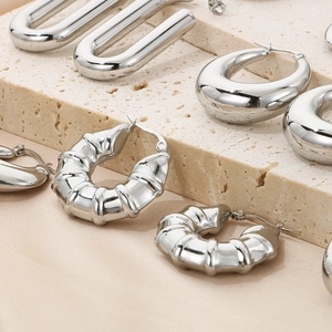Close-up of polished silver U-shape and textured hoop earrings on stone background