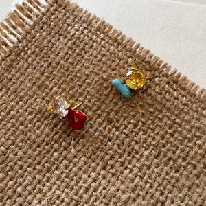 Close-up of asymmetric zircon stud earrings with colorful enameled letter charms.