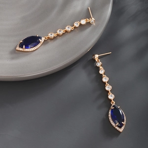 Macro shot of long gold earrings with marquise-cut blue gems and white zircon inlay