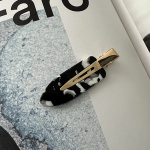 Detail of acetate marble pattern hair clip with gold metal base on minimalist background