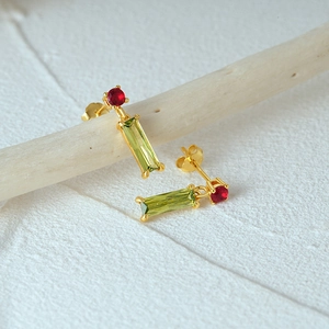 Detailed macro view of gold-plated silver earrings with red and green gemstone pendants