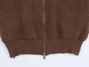 Close-up of brown boucle bomber jacket showing metal zipper and ribbed hem texture