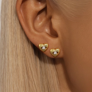 Close-up of a golden heart stud earring with a square zircon on a female model