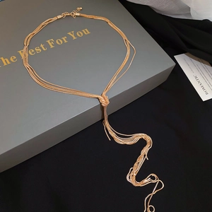 Detail of a gold multi-layer snake chain necklace with a knotted tassel on a gift box