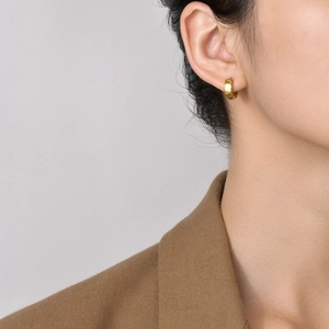 Close-up of golden wide-band hoop earrings on model in minimalist urban style