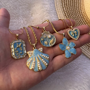 Five gold necklaces with blue enamel ocean charms including shells and birds on palm