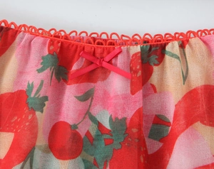 Dettaglio del tessuto con stampa fragole rosse con pizzo e piccolo fiocco di raso