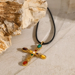 Detailed shot of a gold cross pendant with colorful gemstones and pearl on natural rock