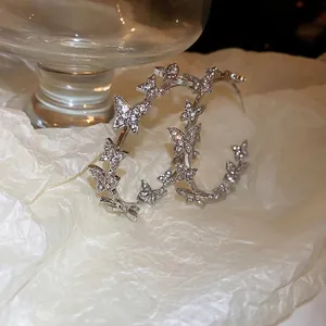 Elegant silver butterfly hoop earrings with sparkling rhinestones on textured background