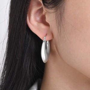Close-up of polished silver hollow hoop earrings worn by a model in a minimal style