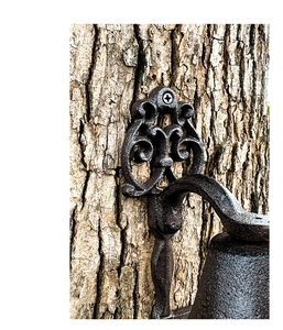 Close-up of vintage cast iron door bell bracket with rustic scrollwork on bark backdrop