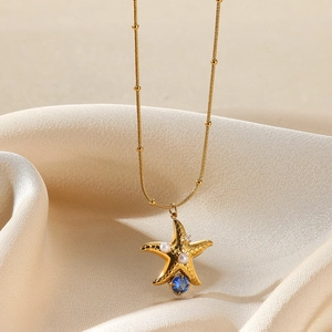 Detailed close-up of a gold starfish necklace with white pearls and blue gemstone on silk