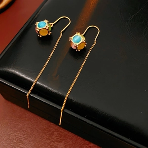 Detailed close-up of gold-plated thread earrings with colorful beads on a black box