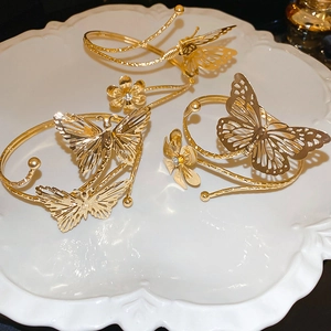 Three-piece gold hollow flower and butterfly metal bracelet set on a white ceramic plate