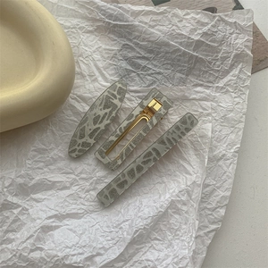 Flat lay detail of grey marble texture hair clips on white paper background