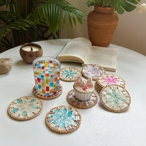 Handcrafted rattan and shell mosaic coaster with floral pattern on a white table