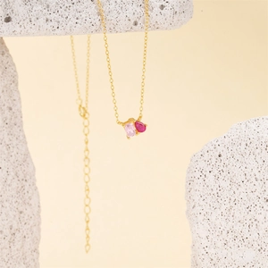 Close-up of golden necklace with pink square and red teardrop zircon stones on a rock