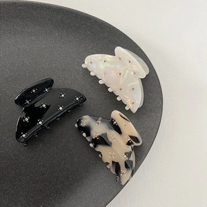 Detail of three acetate hair claws in black, pearl white, and amber with rhinestone flowers