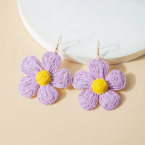 Macro shot of purple and yellow woven raffia flower earrings on a white stand