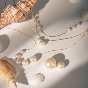 Detail of 18k gold stainless steel necklace with graduated pearls and shells background