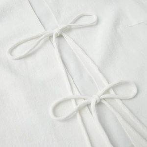 Detailed close-up of pure white sleeveless top with double bow tie design and textured fabric