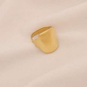 Anello largo geometrico dorato minimalista con bordi irregolari su tessuto beige