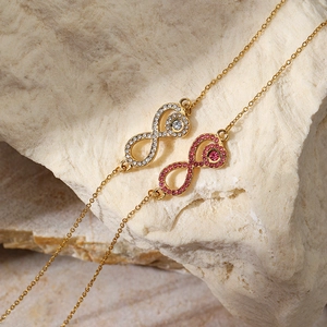Close-up of gold infinity necklaces with pink and white cubic zirconia on white stone