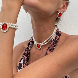 Close-up of vintage jewelry set featuring layered pearls and oval red gemstones on a model