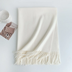 Flat lay of soft white cashmere feel scarf with tassel edge next to a coffee mug
