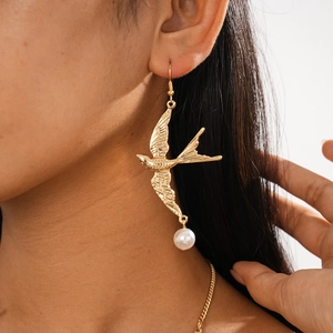 Detailansicht goldener Schwalbenohrringe mit weißen Perlenanhängern an einem Model