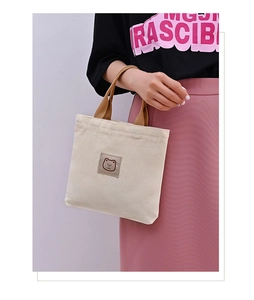 Detail of beige canvas tote bag with brown handles and embroidered cartoon bear