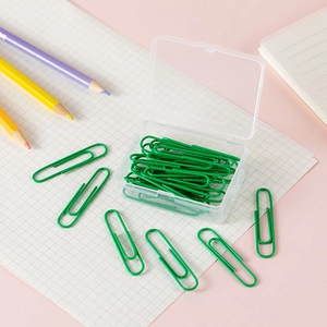 Green coated metal paperclips in a transparent storage box on a pastel pink desk