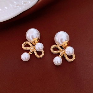 Macro shot of gold bow-shaped pearl earrings with white pearls on a dark background