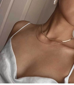 Detail of layered gold flat snake bone chain and thin necklace on a female neck