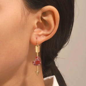 Close-up of golden heart and arrow dangle earring with sparkling pink and red crystals