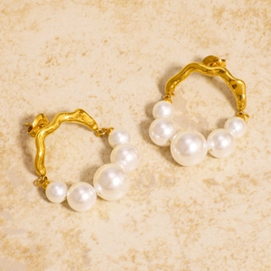 Minimalist gold stainless steel irregular earrings with white pearls on a warm texture