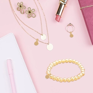 Flat lay of gold fashion jewelry set with floral earrings and beaded bracelet on pink background