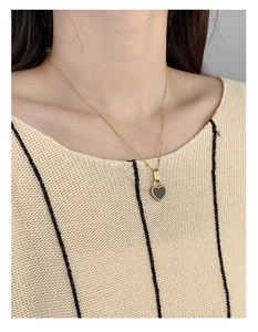 Detail of a minimalist gold heart pendant with black enamel inlay on a beaded chain