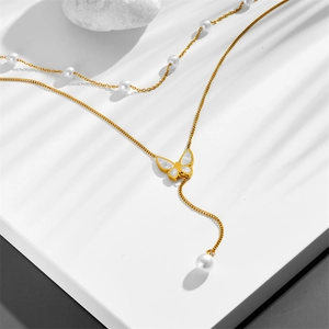 Double-layer gold butterfly necklace with pearls and tassels on white stone surface