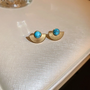 Macro view of gold vintage fan-shaped stud earrings with turquoise stones on white leather