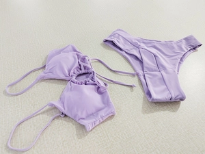 Flat lay of light purple halter bikini set with drawstring bow detail on textured surface