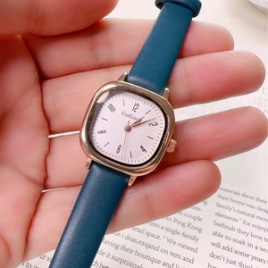 Close-up of a vintage square quartz watch with a gold case and dark blue leather strap