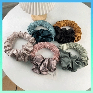 Flat lay of multiple colorful satin silk scrunchies in champagne and pink on white table
