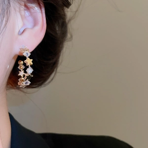 Close-up of a gold C-shaped hoop earring with sparkling star-shaped zircon on a model